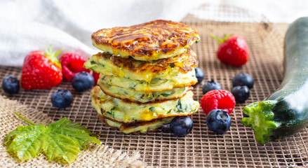 Fresh pile of delicious homemade courgette pancakes topped with honey maple syrup, summer fruits, zucchini and maple leaf on kitchen grill. Close up. Recipe, cooking, season, menu concept