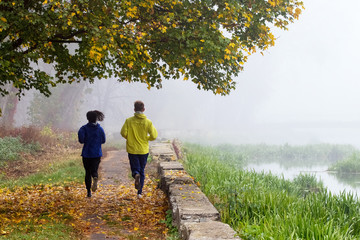 Two young men, a guy and a girl, have a morning run in the autumn park. Morning fog in the park