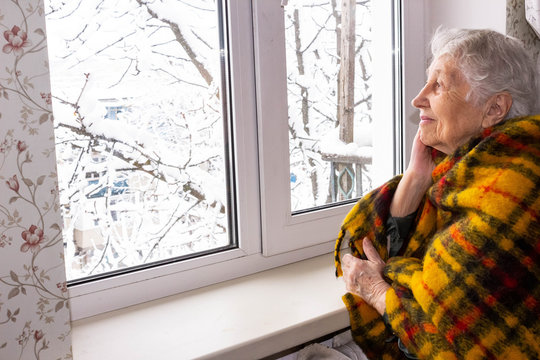 Old lonely woman sitting near the window in his house.