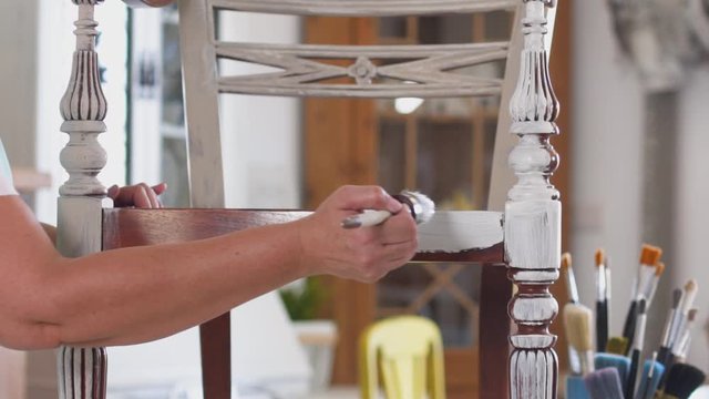 Close-up of craftswoman carpenter repainting old ornate furniture with brush
