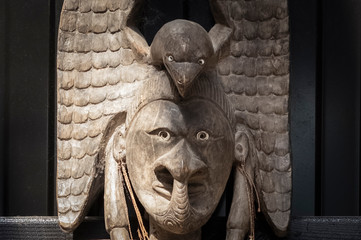 Detail of a totem pole made of wood. Bird on the man head. Ritual attribute. Close-up