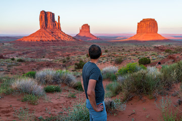 Man tourist standing looking at view of famous buttes and horizon in Monument Valley at sunset...
