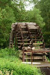 An old weathered mill wheel made of wood, in the middle of green vegetation in portrait format