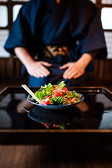 Traditional japanese room in ryokan restaurant house with black lacquered wood table and salad dish with man in kimono or yukata sitting in background