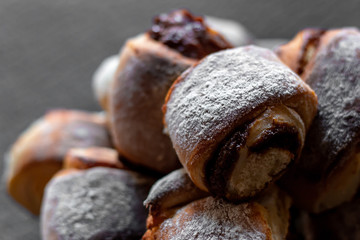 slide of fresh homemade buns with condensed milk and powdered sugar on a plate, on a gray background close-up, macro