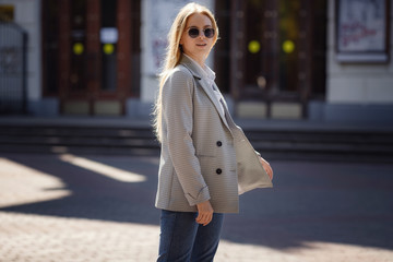 Sunny lifestyle fashion portrait of a young stylish hipster woman walking in the city, wearing a fashionable outfit