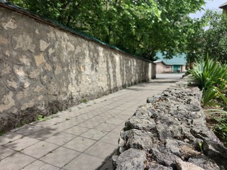 The stone wall of an Orthodox monastery. Green plants, Stone steps. Blue sky.