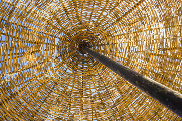 Low angle, below view of a wicker umbrella on the beach. Close up of a wicker beach umbrella on a sunny day, sky in background. 