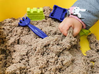 A child plays with kinetic sand: closeup of a child's hand and sand. Sand in a yellow container...