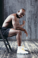 A muscular dark-skinned man sits and shows his biceps hard. Healthy lifestyle concept