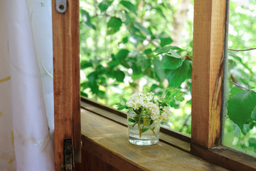 open window in a old wooden house with white flowers bouquet. summer blooming view. green garden over the window. house in a garden. countryside calm place