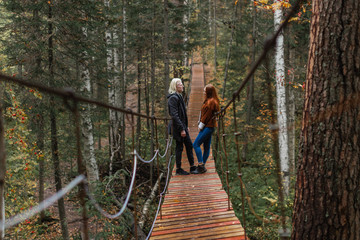 A young albino guy and a red-haired girl stand on in the woods on a suspension bridge and look at each other 