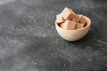 cane sugar cubes in a wooden bowl. Unrefined brown cane sugar. grey background with copy space for text.