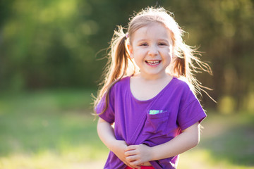 cute child laughing outdoor in summer. happy girl in setting sun against background of green trees. activity in Park. sportswear for children