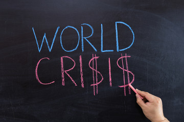 The concept of the world crisis on the blackboard. Hand with chalk.