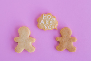 Fototapeta premium Homemade shortbread cookies with white glaze on pink background, top view. Two people with callout cloud with text ‘How are you?’