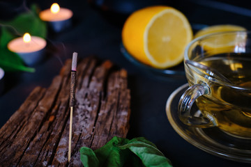 Close-up of incense stick, candles, lemon and cup of green tea