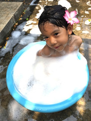 Little girl is  playing outdoor in blue plastic tub which full of bath foam,  she enjoys her free time when have to stay at home because of Coronavirus 19. 
