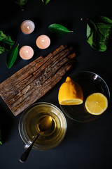 Green tea cup, incense stick, candles and lemons on black table