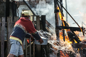 Man tries to put out a fire at a slum with a bucket of water.