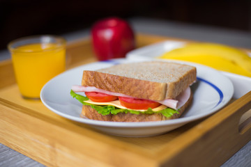 Close-up of breakfast made with a ham sandwich, orange juice, a banana and an apple on a wood plate...
