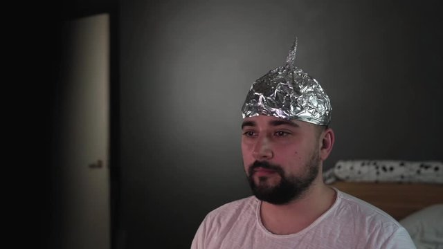 Suspicious bearded man in tin foil hat watching white noise on TV screens at home.
