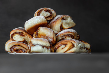 slide of fresh homemade buns with condensed milk and powdered sugar on a plate, on a gray background