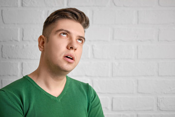 Confused rolls his eyes up, hands folded on his chest. Portrait of a handsome caucasian man. Brick wall background. Studio photo.