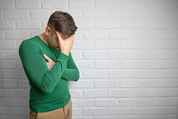 Portrait of young man with face palm gesture. Disappointed stressed out male making facepalm with hand. Brick wall background. Studio photo. There is a place to copy space.