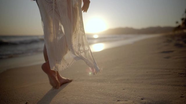 Close up of young woman's feet walking barefoot along beach as sun sets in the distance in Mexico
