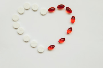 Heart of white tablets and red capsules on a white background. Figure of tablets. The heart is a symbol of love.