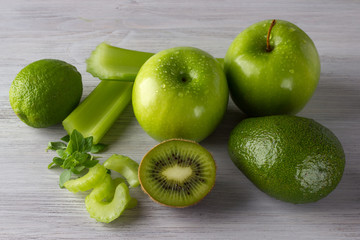 Fototapeta na wymiar Fresh green fruits and vegetables: apples, lime, kiwi, basil, avocado, celery on the white wooden table
