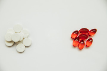 White tablets and red capsules lie separately in different piles on a white background. Pharmaceutical production of medicines.