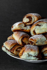 slide of fresh homemade buns with condensed milk and powdered sugar on a plate, on a gray background close-up, macro