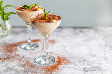 Tasty Italian tiramisu decorated with mint in a glass on a grey background. Copy space.