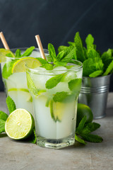 Two homemade lemonade or mojito cocktail with lime, mint and ice cubes in a glass on a dark stone table. Fresh summer drink