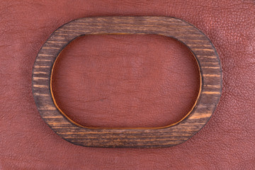 Oval wooden frame made of wood lies on brown genuine leather. Top view.