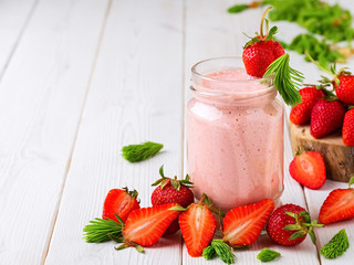 Strawberry cocktail in a glass jar on a wooden white table. Strawberries and spruce tips, smoothie ingredients scattered on the table. Close-up with copy space.