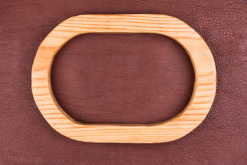 Oval wooden frame made of wood lies on brown genuine leather. Top view.