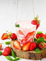 Strawberry cocktail in a glass on a wooden stand, white wooden background. Strawberries and spruce tips scattered on the table, ingredients for making smoothies. Close-up with copy space.