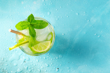 Homemade lemonade or mojito cocktail with lime, mint and ice cubes in a glass on a light stone...