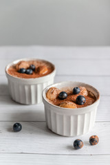 Classic tiramisu dessert with blueberries in white cup on grey concrete background. Vertical photo
