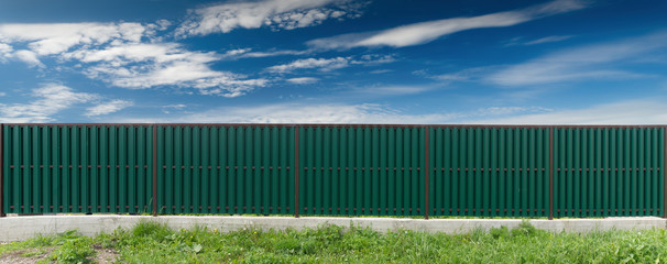 Green metal fence. The sky with clouds.