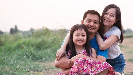 Happy joyful asian family father, mother and little daughter smiling and hugging, enjoying nature outside.