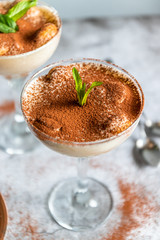 Tasty tiramisu in glass, mint leaves and strainer with cocoa on gray background, vertical