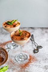 Close up of a traditional Italian sweet tiramisu cake dessert with mint and blueberry berries in glass on grey. Vertical photo