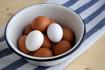 The curine raw eggs are in a enameled bowl. Eggs are white and brown. Bowl is on kitchen napkin, on wooden table.