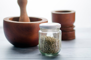White Pepper in a glass jar on white background/wooden ponders in the backdrop.