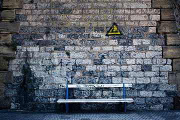 Muro de piedra con grafiti y un banco