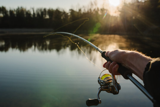 Fisherman with rod, spinning reel on the river bank. Sunrise. Fishing for pike, perch, carp. Fog against the backdrop of lake. background Misty morning. wild nature. The concept of a rural getaway.